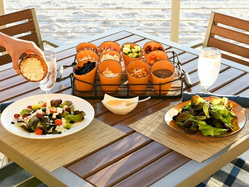 Person pouring feta cheese on to a salad