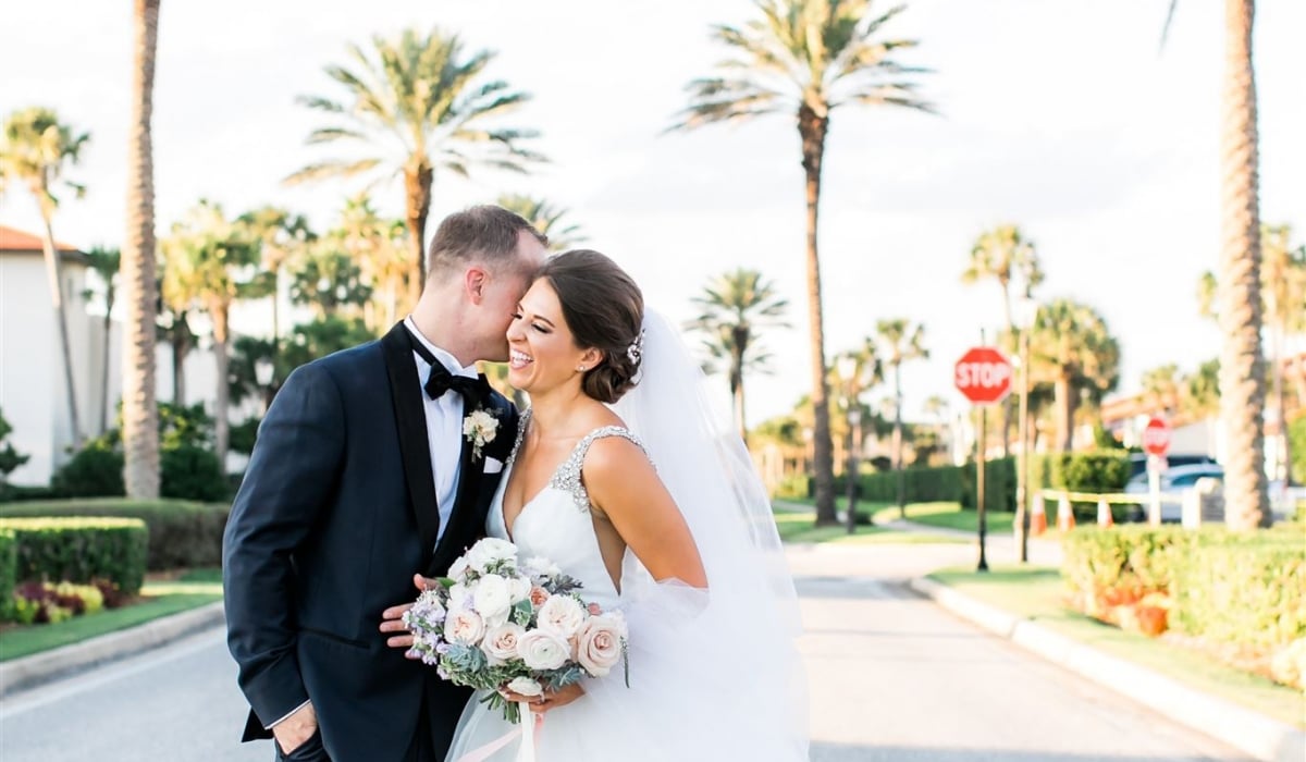 A bride and groom smile as they stand the street under palm trees at Ponte Vedra Inn & Club.