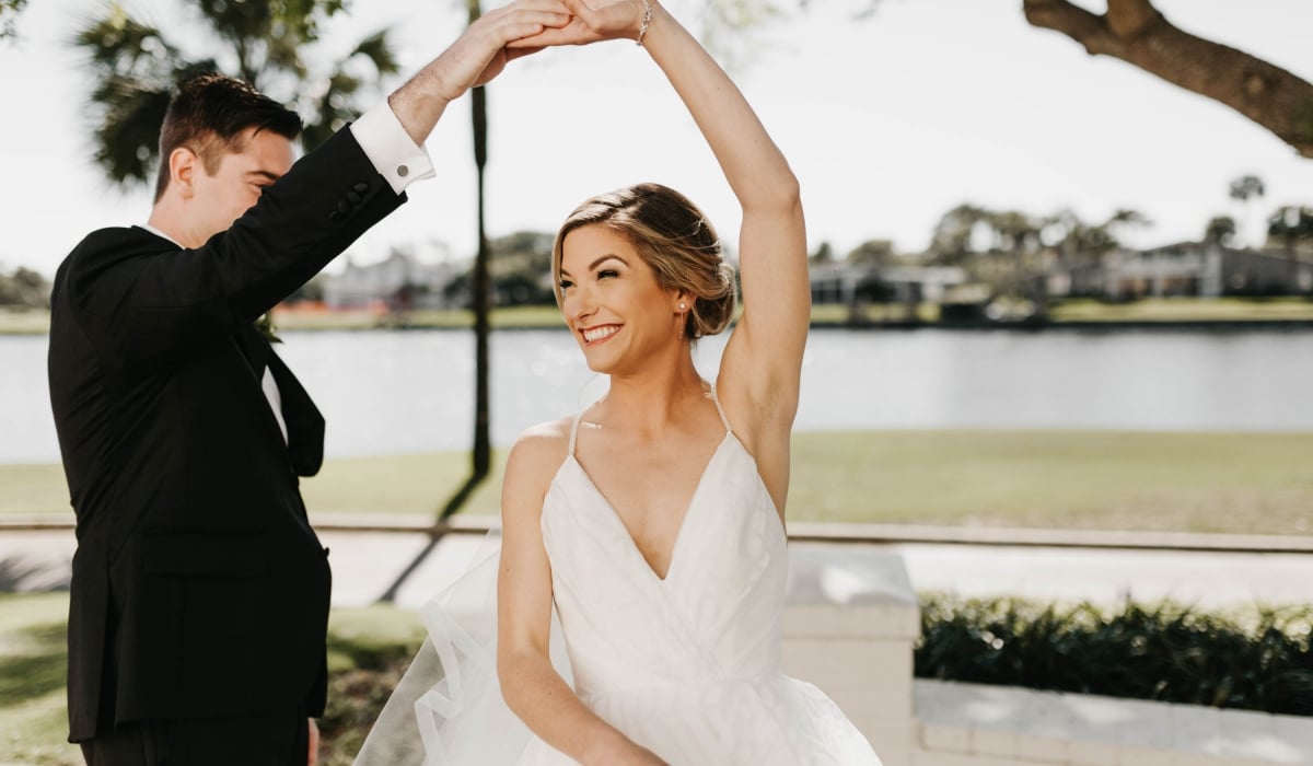 A groom twirls his bride under a tree with the lagoon in the background at Ponte Vedra Inn & Club